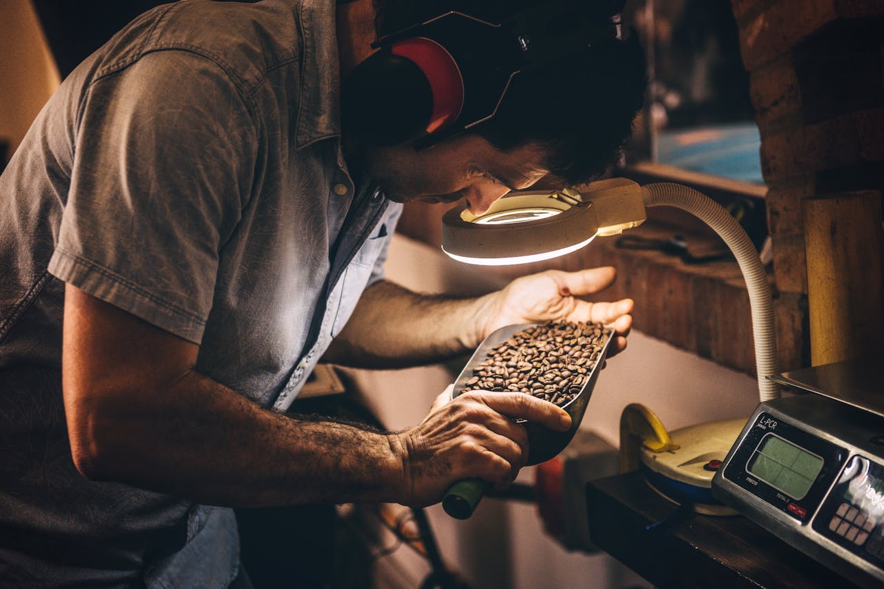 about-01 A man carefully inspects coffee beans under a lamp, showcasing the artisan process in Playa del Carmen.